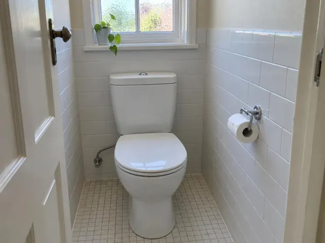 Clean white toilet in a tiled bathroom with a window and toilet roll holder in Kogarah